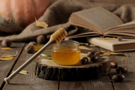 Autumn composition with honey close-up and acorns on a wooden stand on a brown wooden tableの写真素材