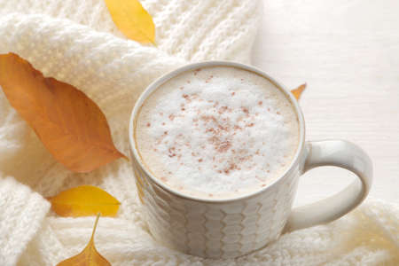 Autumn composition with hot coffee, a warm scarf and yellow leaves on a white wooden tableの写真素材