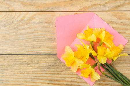 A bouquet of daffodils, spring flowers and a pink envelope. on a natural wooden background. top viewの写真素材