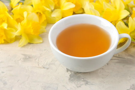 Spring flowers, yellow daffodils and a cup of tea on a light concrete background.の写真素材