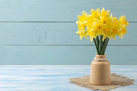 Spring flowers, yellow daffodils in a vase on a blue wooden background. place for textの写真素材