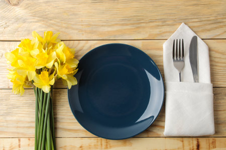 Table setting and spring flowers, yellow daffodils. Plate, knife and fork on a natural wooden table. top viewの写真素材