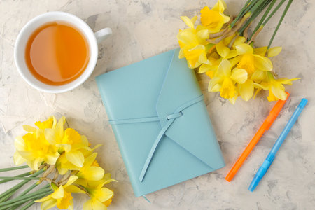 Spring flowers, yellow daffodils and a cup of tea, a notebook on a light concrete background. top viewの写真素材