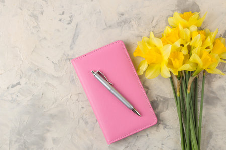 Spring flowers, yellow daffodils and notebook, on a light concrete background. top viewの写真素材