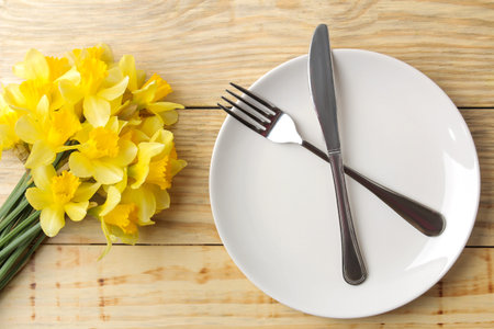 Table setting and spring flowers, yellow daffodils. Plate, knife and fork on a natural wooden table. top viewの写真素材