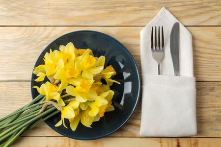 Table setting and spring flowers, yellow daffodils. Plate, knife and fork on a natural wooden table. top viewの写真素材