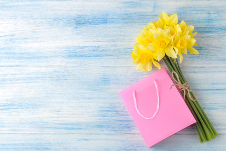 Spring flowers, yellow daffodils and gift bag on a blue wooden background. place for textの写真素材