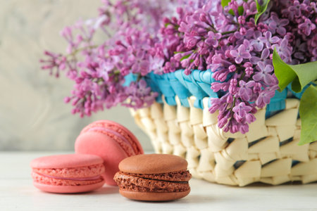 spring flowers. Twigs of blooming lilac in a wicker basket and macaroon cake on a light concrete backgroundの写真素材