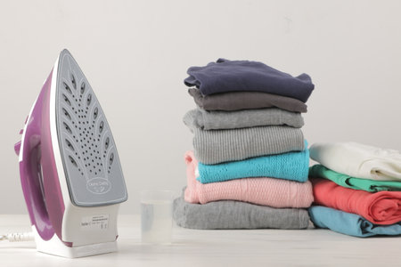 Iron and a stack of colored clothes on a white background. Ironing of clothes after washing and cleaning.の写真素材