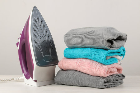 Iron and a stack of colored clothes on a white background. Ironing of clothes after washing and cleaning.の写真素材