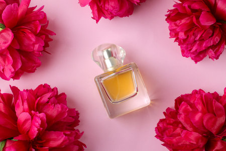 A frame of beautiful bright pink peony flowers on a pale pink background and a bottle of women's perfume. top view.の写真素材