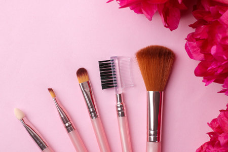 Frame of beautiful bright pink peonies flowers on a pale pink background and makeup brushes. top view.の写真素材