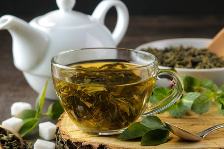 green tea. Hot tea in a cup on a wooden stand, sugar and mint on a dark background.の写真素材