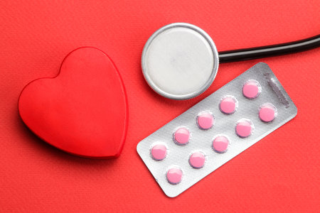 Stethoscope on a red background with pills and a red heart. view from above . heart health and medical care.の写真素材