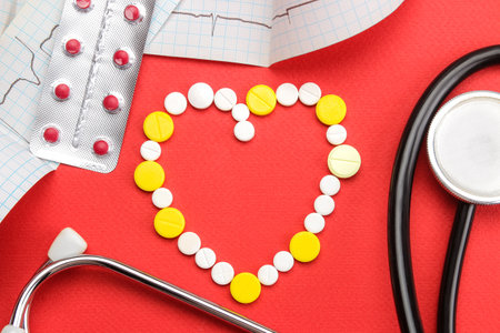 Pill heart, stethoscope and cardiogram on a red background. view from above. cardiology and heart health.の写真素材