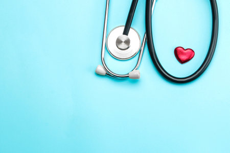 Stethoscope and a small red heart on a blue background. top view and free space. Cardiology and treatment of heart diseases.の写真素材