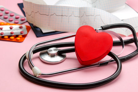 Stethoscope, red heart, cardiogram and various pills on a pink background. doctor's desk. Cardiology and treatment of heart diseases.の写真素材