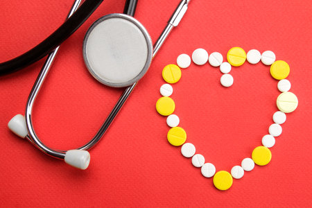 Heart made of pills and a stethoscope on a red background. view from above. cardiology and heart health.の写真素材