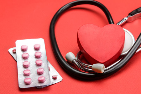 Stethoscope on a red background with pills and a red heart. heart health and medical care.の写真素材