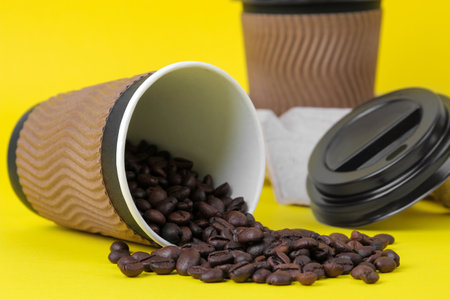 Paper cups with coffee beans on yellow backgroundの写真素材