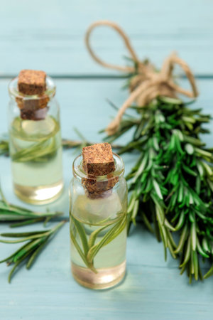 Natural rosemary essential oil in a glass bottle and a fresh sprig of rosemary on a blue table. face and body skincare. spa.の写真素材