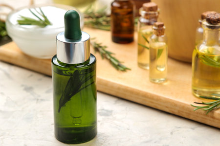 Natural rosemary essential oil in a glass bottle and a fresh sprig of rosemary on a light background. face and body skin care. spa.の写真素材