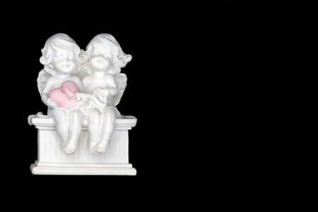 Two angels are sitting on a bench and holding a heart with a key in their handsの写真素材