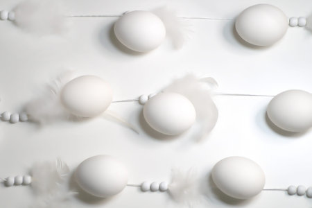 White eggs lie in a row on strings with beads and feathers on a white backgroundの写真素材