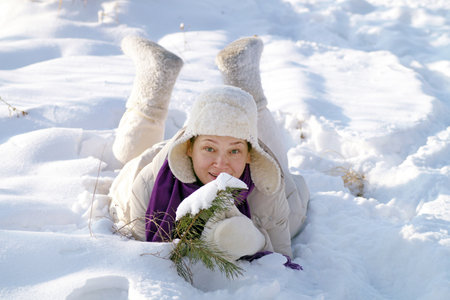 A happy woman lies in front of a small pine tree in the snowの写真素材