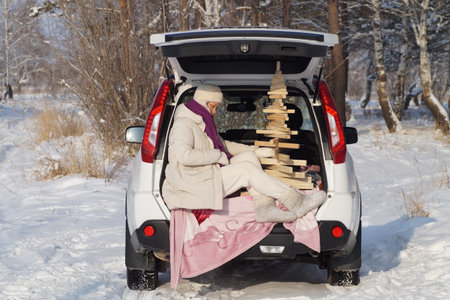 A woman adjusts her scarf and holds an eco-spruce tree in the trunk of a carの写真素材