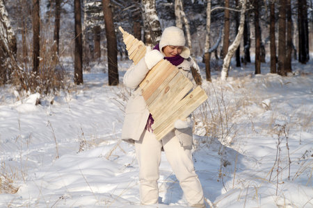 A woman stands in the forest with a wooden Christmas tree in her handsの写真素材