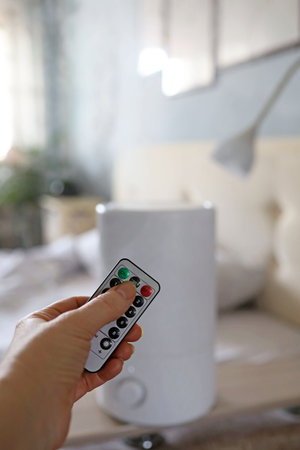A hand with a remote control in front of an air humidifier on a wall backgroundの写真素材