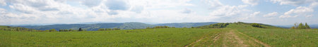 Panoramic view of the Carpathian mountains covered by a green forest under a blue sky and white...
