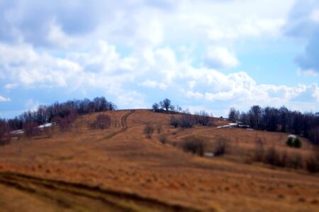 View of autumn mountains with trees without leaves under a cold gray sky and heavy white cloudsの写真素材