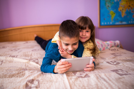 brother and sister using a digital tablet while lying on the bed at home  Brother and Sister Having Fun with tablet at homeの写真素材