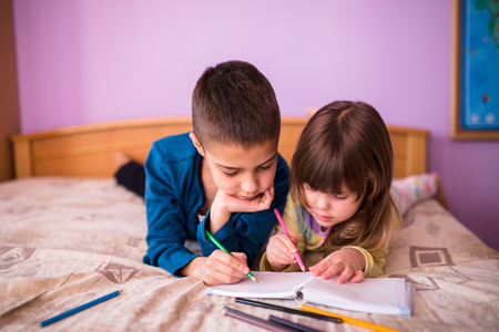 Sister and brother drawing colorful pencils, lying down on the bed  Brother and Sister Having Fun drawing at bedの写真素材