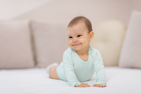 Baby girl on white bed. Cute baby girl lying on her tummyの写真素材