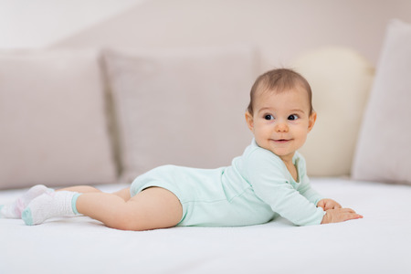 Baby girl on white bed. Cute baby girl lying on her tummyの写真素材