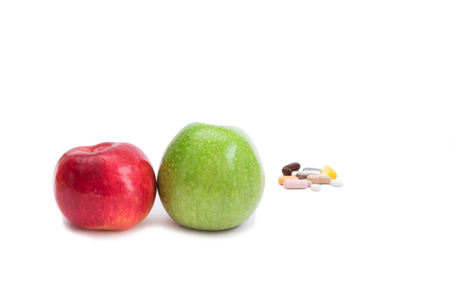 Green and red apples on foreground and group of pills on background, focus on applesの写真素材