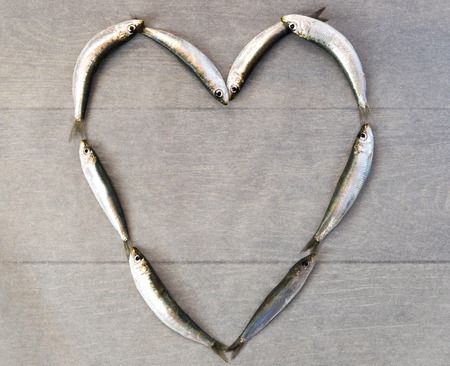 Fresh sardine laying in heart form on wooden tableの写真素材