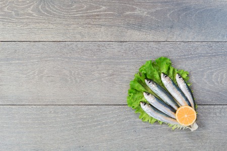 Five fresh sardines in heart form laying on green lettuce with slice of lemon, wooden tableの写真素材