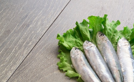 Four fresh sardines on green lettuce, wooden tableの写真素材