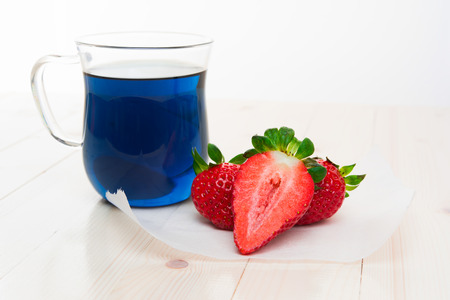 Blue Thai tea and strawberries on parchment, light wooden table, bright daylight.の写真素材