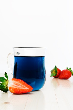 Blue Thai tea and strawberries, light wooden table, bright daylight.の写真素材