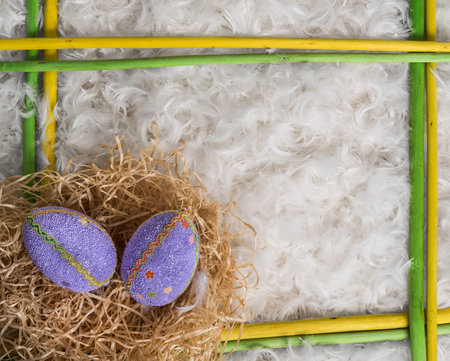 Two Easter eggs in yellow and green wooden frame on background from small feathers