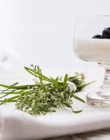 Small bouquet of wild grass, glass with yogurt and blueberry from side. Focus on bouquetの写真素材