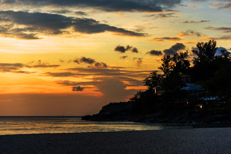 Orange sunset with sea and silhouette of land, couple lights of house between treesの写真素材