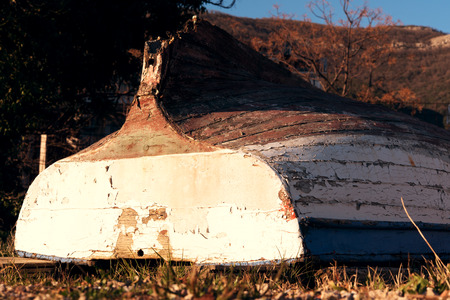 Old boat with cracked paint upturned on grass, sunsetの写真素材