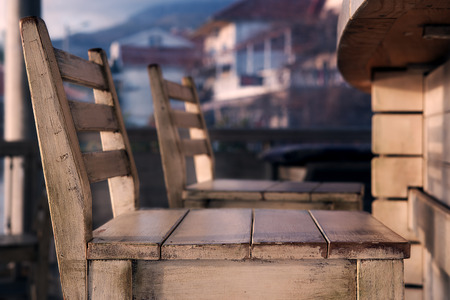 Empty seats in seaside cafe, old wood with white paint, sunset. Buildings on background. Tonedの写真素材