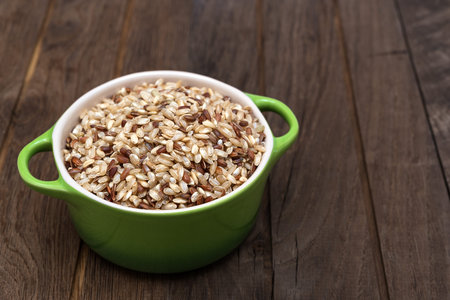 Raw brown rice in ceramic pot on wooden backgroundの写真素材